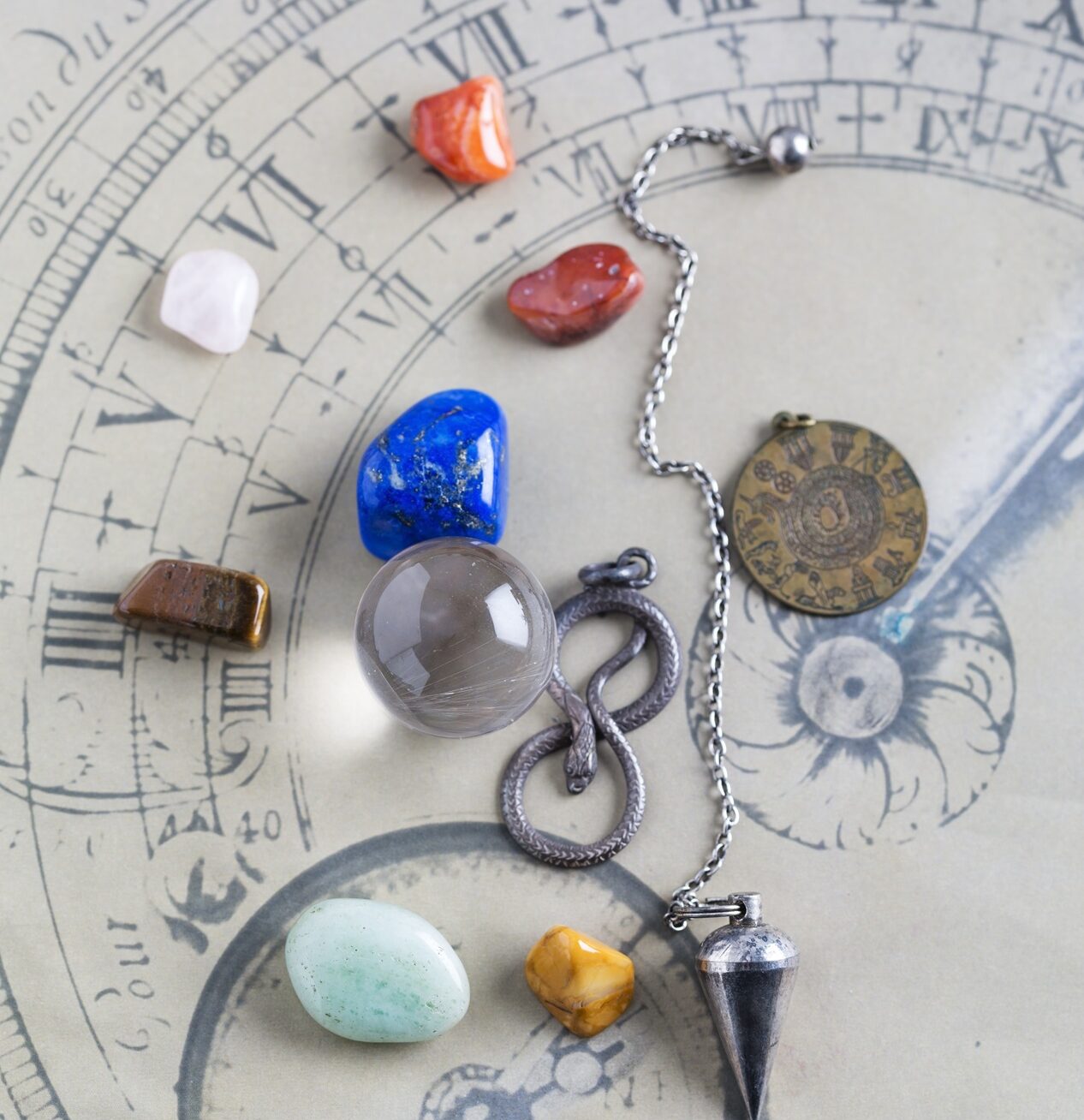 Semiprecious stones, pendulum, pendant and crystal ball on horoscope circle